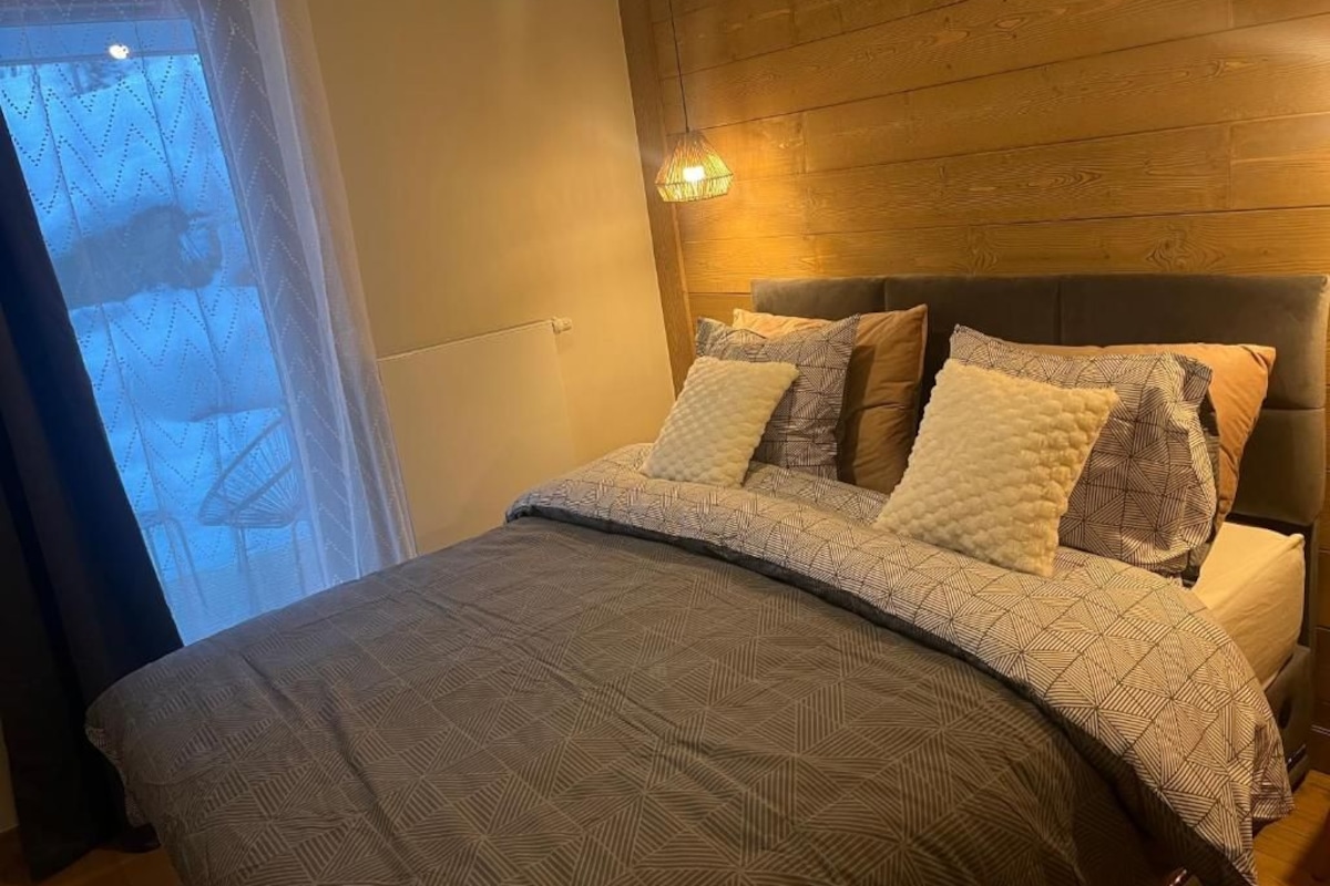 A bedroom with a bed, a headboard, and a window with curtains.