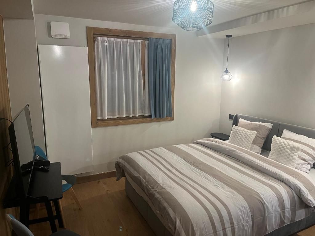 Un dormitorio con cama, escritorio, silla, ventana con cortinas e iluminación en el techo.