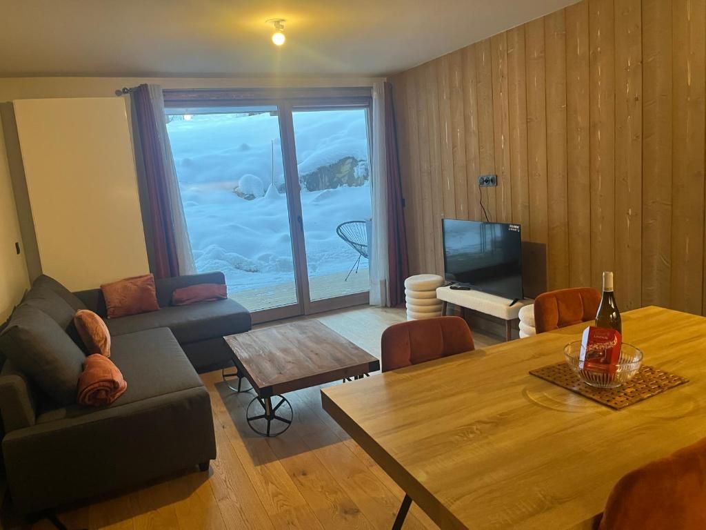 Ein Wohnzimmer mit einer Couch, einem Fernseher, einem Esstisch und Blick auf eine verschneite Landschaft durch die Glasdoor.
