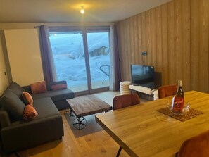 A living room with a sofa, a TV, a dining table, and a view of a snowy landscape through the glass door.