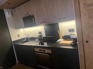 A compact kitchen with a black countertop, wooden cabinets, a built-in microwave, and a coffee machine.