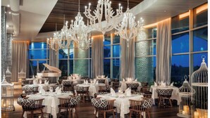 A spacious dining area with multiple tables, elegant chandeliers, and large windows offering a view of the night sky. - One Bedroom Suite Grand Mayan, Vidanta's Luxury Beach Resort, VIP Theme Park acc (Nuevo Vallarta)