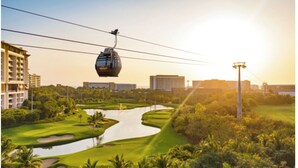 A cable car over a golf course with a water feature, surrounded by greenery and buildings. - One Bedroom Suite Grand Mayan, Vidanta's Luxury Beach Resort, VIP Theme Park acc (Nuevo Vallarta)