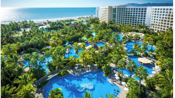 A resort with multiple swimming pools surrounded by palm trees, a beach, and a large hotel building. - One Bedroom Suite Grand Mayan, Vidanta's Luxury Beach Resort, VIP Theme Park acc (Nuevo Vallarta)