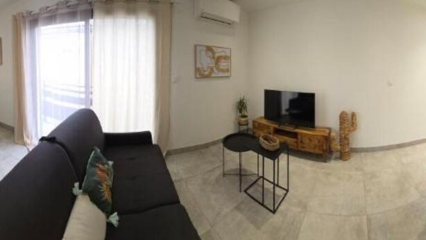 A modern living room with a black sofa, a small table, and a television. - 200 m from the beach - Quiet apartment with balcony and garage num4 (Le Grau-du-Roi)