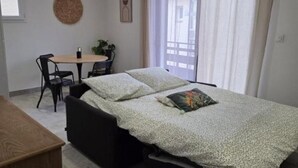 A bedroom with a bed, a small table, a chair, and a window with curtains. - 200 m from the beach - Quiet apartment with balcony and garage num4 (Le Grau-du-Roi)