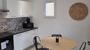 A modern kitchen with white cabinets, a black countertop, and a round wooden table. - 200 m from the beach - Quiet apartment with balcony and garage num4 (Le Grau-du-Roi)