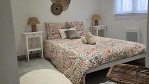 A bedroom with a patterned bedspread, two bedside tables with lamps, a wall hanging, and a window with curtains. - 200 m from the beach - Quiet apartment with balcony and garage num4 (Le Grau-du-Roi)