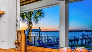 Un comptoir de bar en bois offrant une vue sur un coucher de soleil sur l’eau, un palmier et des chaises longues.