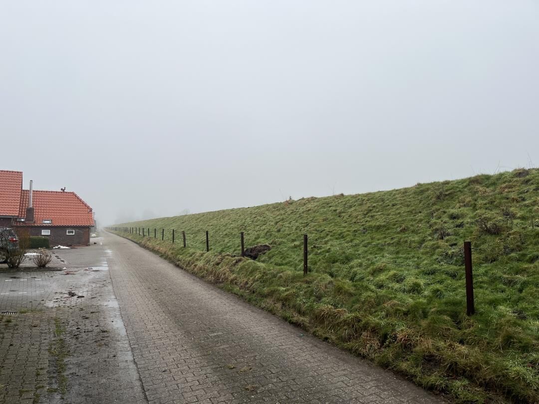 A rural road with a house on the left and a grassy hill on the right.