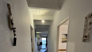 Ein schmaler Korridor mit Holzboden führt zu einem Schlafzimmer mit Bett und Fenster.
