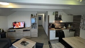 Eine moderne Küche mit Essbereich, ein Fernseher im Wohnzimmer und ein sichtbarer Flur, der in ein weiteres Zimmer führt.