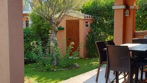 Eine Terrasse mit Tisch und Stühlen, umgeben von einem Garten mit verschiedenen Pflanzen und Blumen.