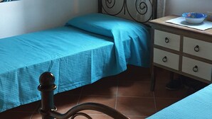 Ein Schlafzimmer mit zwei Betten, einem Fenster mit Jalousien, einem Bild an der Wand und einem Nachttisch mit einer Schale.