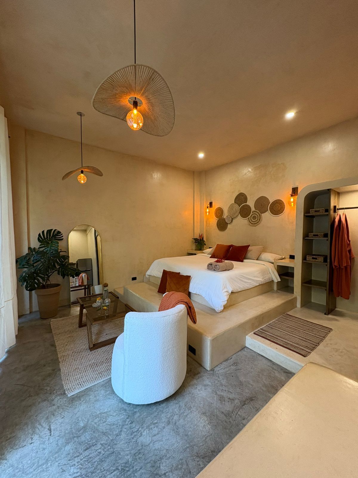 Un dormitorio moderno con una cama grande, una zona de estar con una silla, una mesita y una planta en maceta.