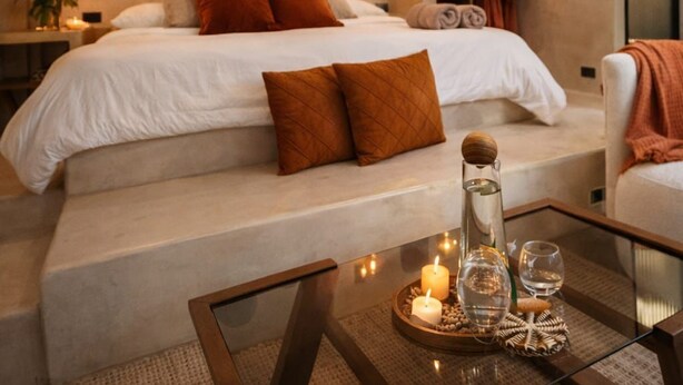 A modern bedroom with a large bed, a glass coffee table with candles, and a view of the bathroom. - The Hidden Garden (San Marcos La Laguna)