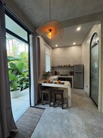 Una cocina moderna con una isla central, una lámpara colgante y vistas al exterior con vegetación.