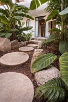 Un sendero en un jardín con escalones circulares de piedra, rodeado de rocas grandes y plantas tropicales.