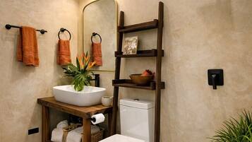 Un baño moderno con un espejo grande, un inodoro blanco y un estante de madera con toallas y artículos de aseo.