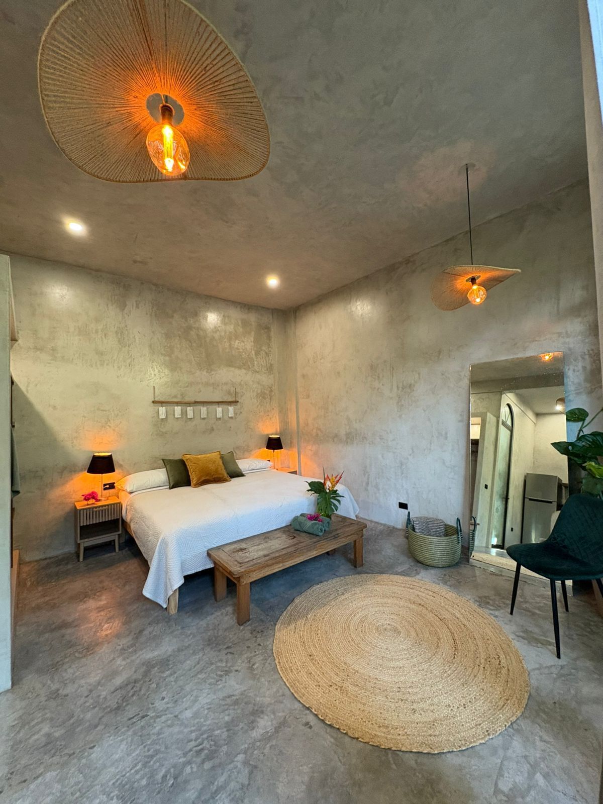 A modern bedroom with a bed, bedside lamps, a wooden bench, a woven rug, and a hanging light fixture.