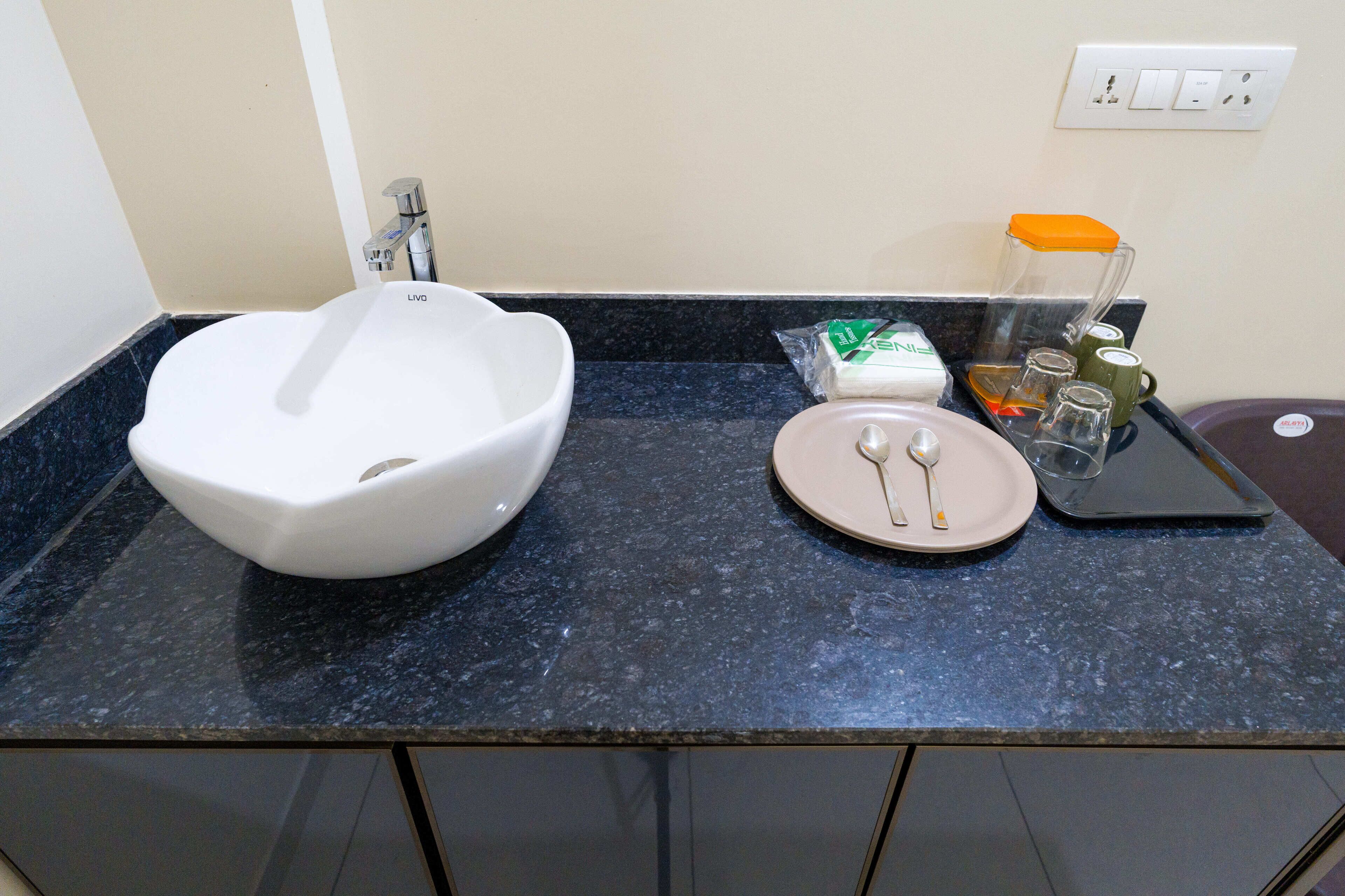 Un lavamanos de baño con un lavabo blanco, un dispensador de jabón, un portalapices para cepillos de dientes y un afeitador.