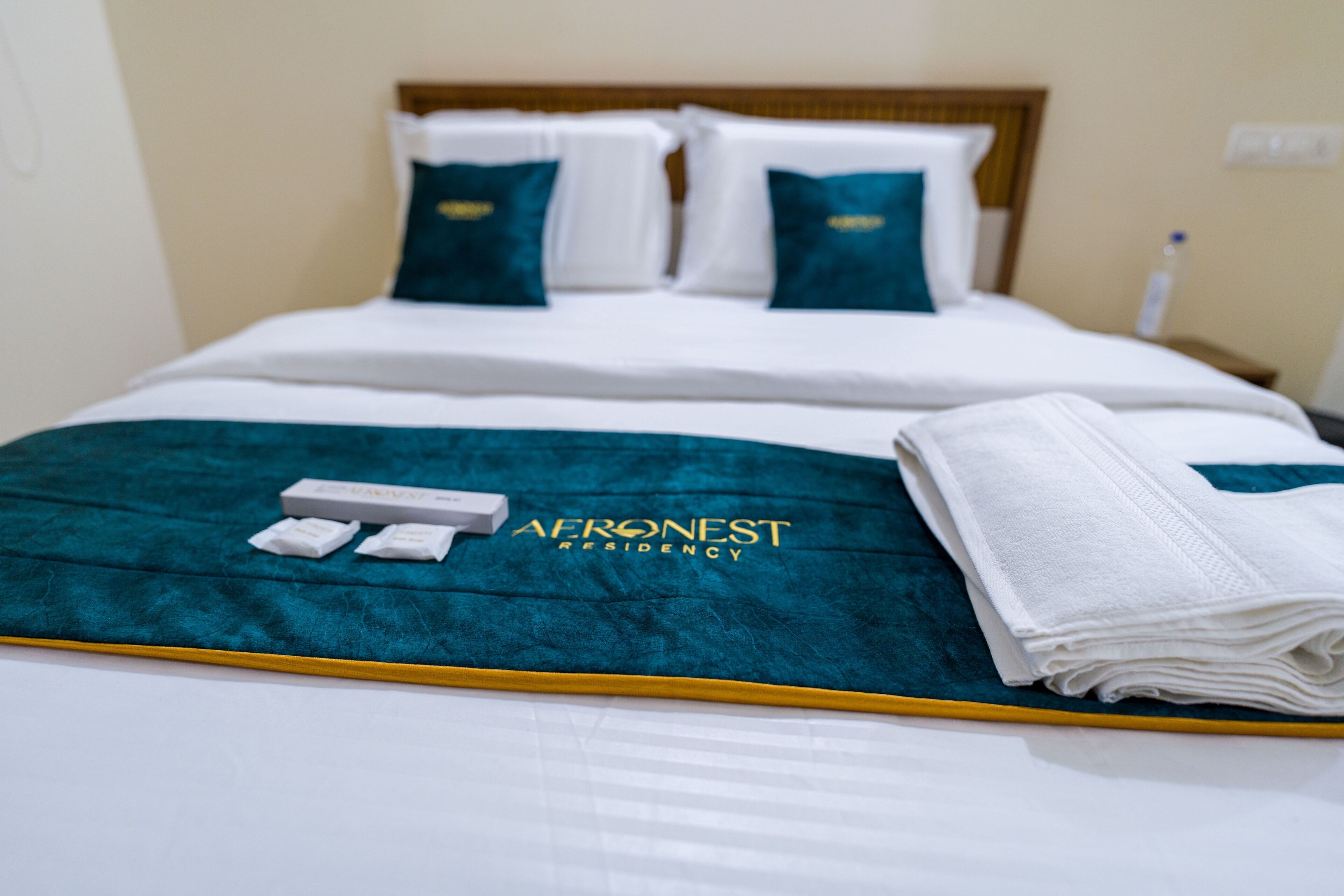 Una cama bien hecha con una colcha color turquesa, almohadas blancas y una toalla blanca doblada.