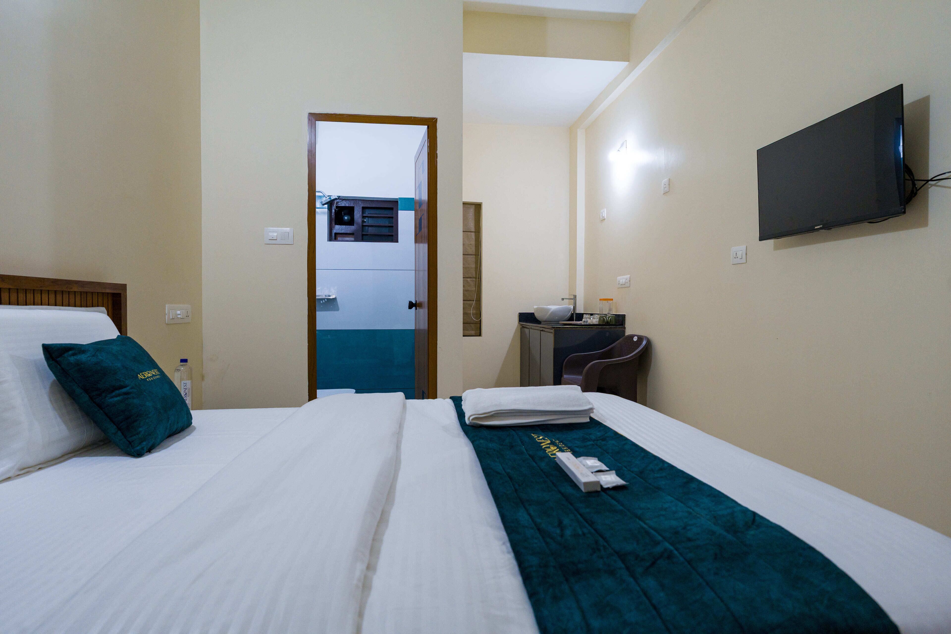 Una habitación de hotel con una cama, un televisor montado en la pared y un escritorio con una silla.
