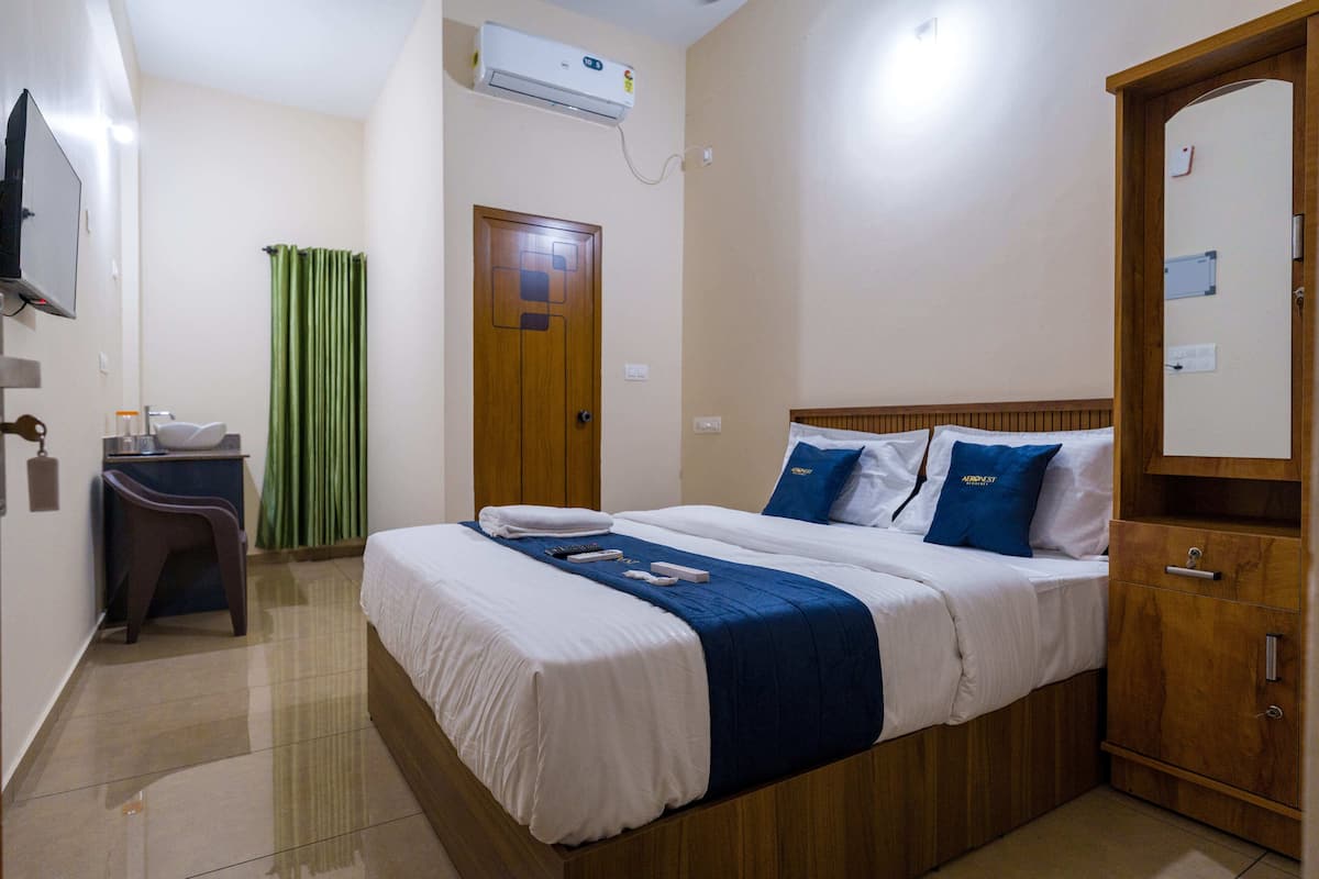 A hotel room with a bed, a desk, a chair, a wardrobe, and an air conditioning unit.