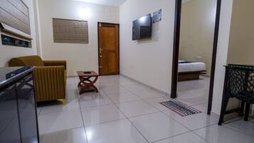 Una habitación con cama, televisión montada en la pared, puerta de madera y ventana con persianas.