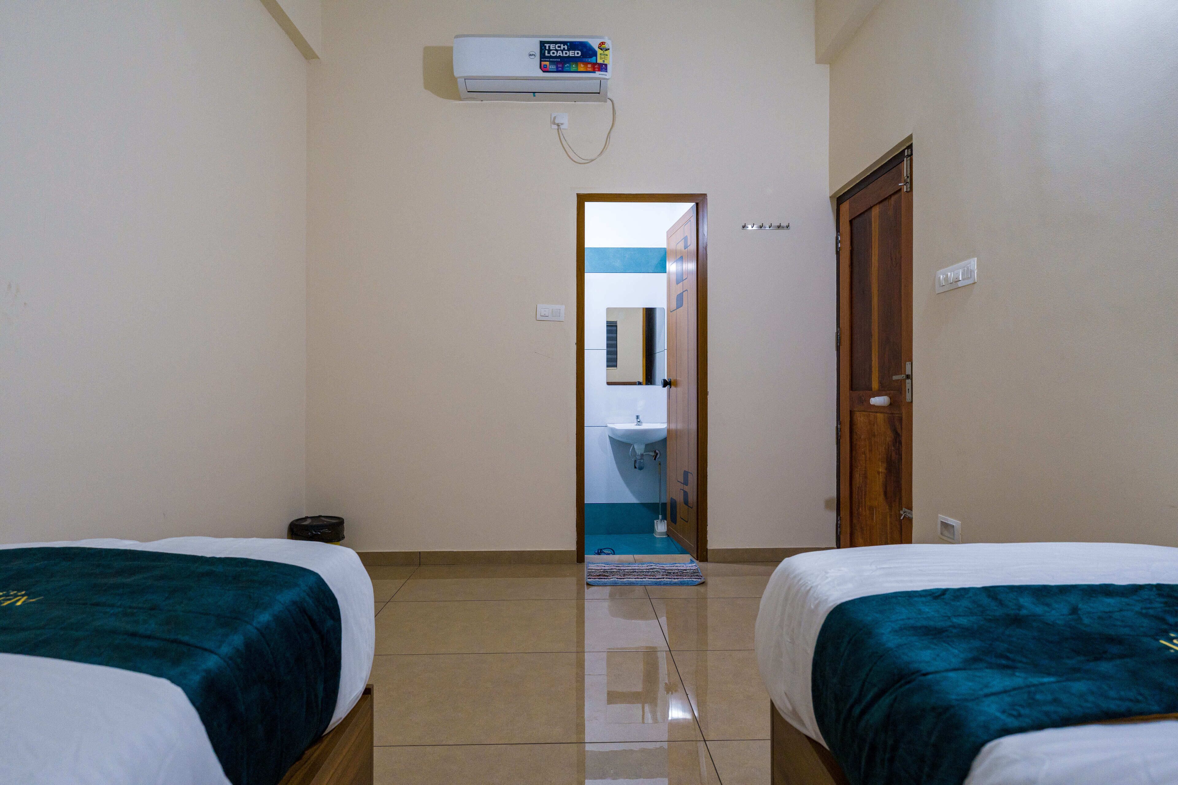 A hotel room with two beds, a bathroom visible through an open door, and a ceiling air conditioner.