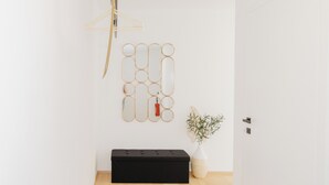 Et minimalistisk rum med en sort bænk, et spejl på væggen og en lille plante.