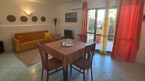 Un comedor con una mesa y sillas, un sofá, un cuadro en la pared y una ventana con cortinas.