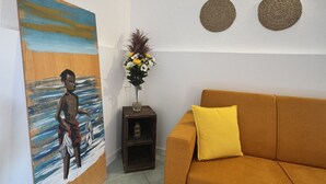 Una habitación con un sofá marrón, un cuadro de una persona, un jarrón con flores y dos adornos tejidos para la pared.