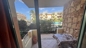 Un balcón con una mesa y sillas, un cilindro de gas y vistas a un edificio de hotel con varios balcones y una piscina.