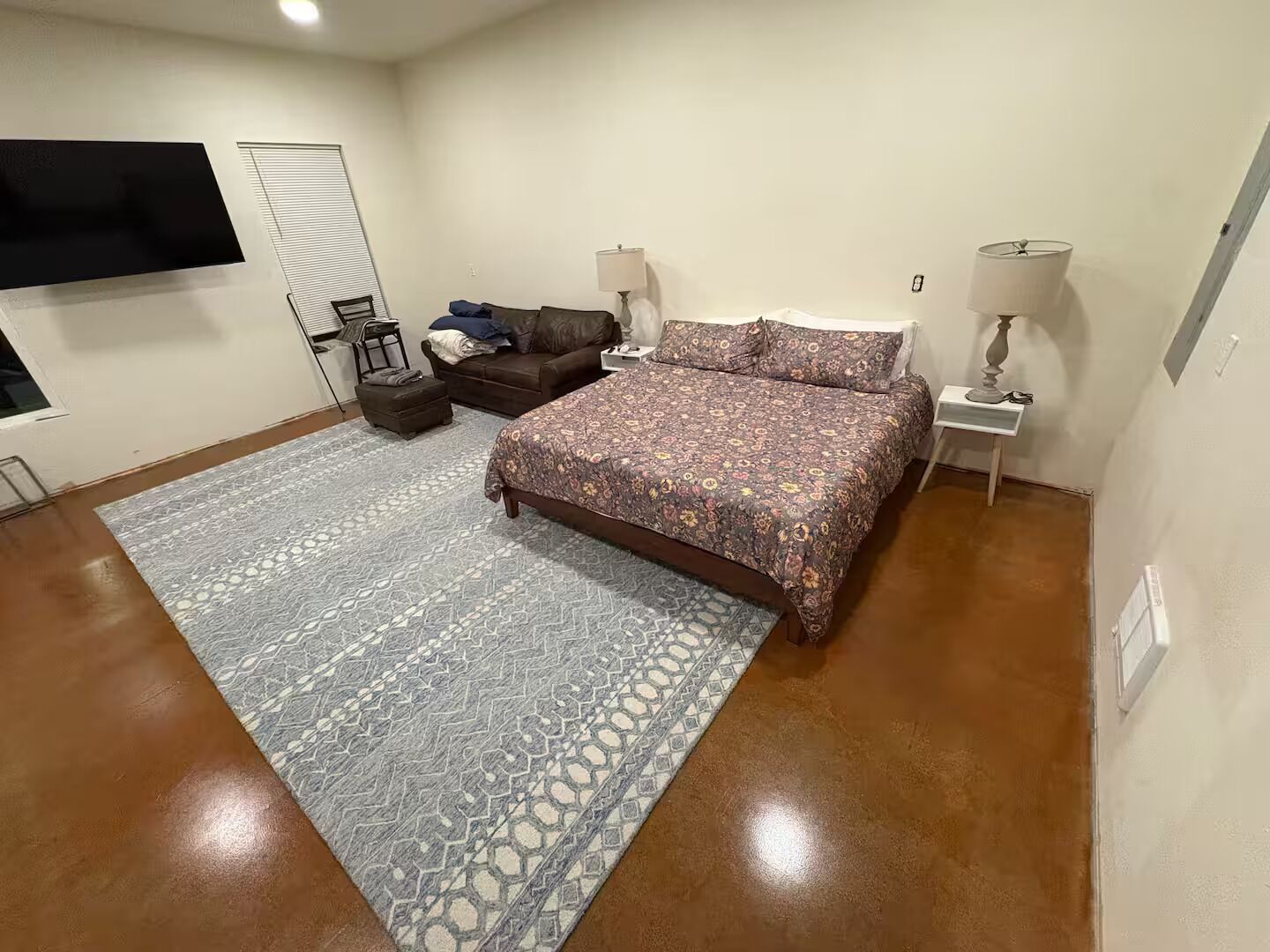 Ein Schlafzimmer mit einem Bett, einer Couch, einem kleinen Tisch, einer Lampe und einem an der Wand befestigten Fernseher.