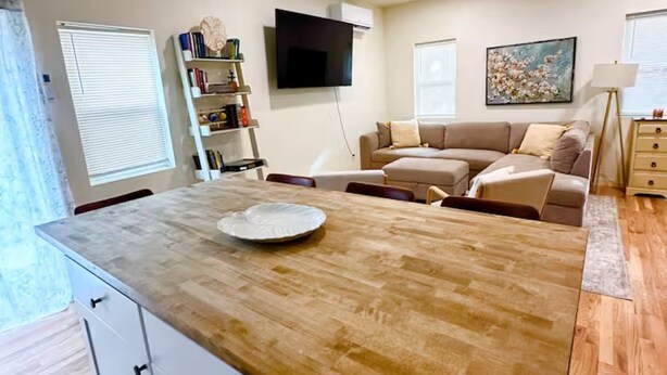Uma sala de estar moderna com uma ilha de madeira, uma TV de tela plana, um sofá e uma área de jantar com mesa.
