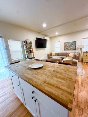 A modern living room with a wooden island, a flat-screen TV, a sofa, and a dining area with a table.