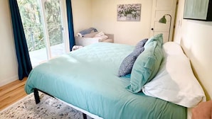 Quarto com cama, mesa de cabeceira, porta e janela com cortinas.