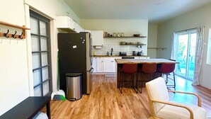 Uma sala ampla com piso de madeira, uma mesa de jantar com cadeiras, um sofá e uma cozinha com armários brancos e uma geladeira.