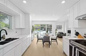Une cuisine moderne avec des meubles blancs, un îlot central doté de sièges et une vue sur une piscine et un espace extérieur.
