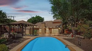 Ein Garten mit Pool, einer überdachten Terrasse und einem Haus mit Backsteinfassade.