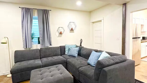 Ein modernes Wohnzimmer mit einem grauen Ecksofa, einem passenden Ottomanen und einem gemusterten Teppich.