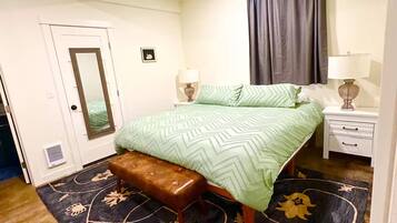 A bedroom with a bed, bench, bedside tables, a mirror, and a window with curtains.