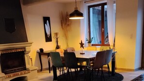 Olohuone, jossa on takka, ruokapöytä tuoleineen, kattokruunu ja shakkilauta.