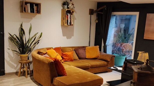 Moderni olohuone, jossa on kulmasohva, pieni puujakkara, ruukkukasvi ja kirjahylly.