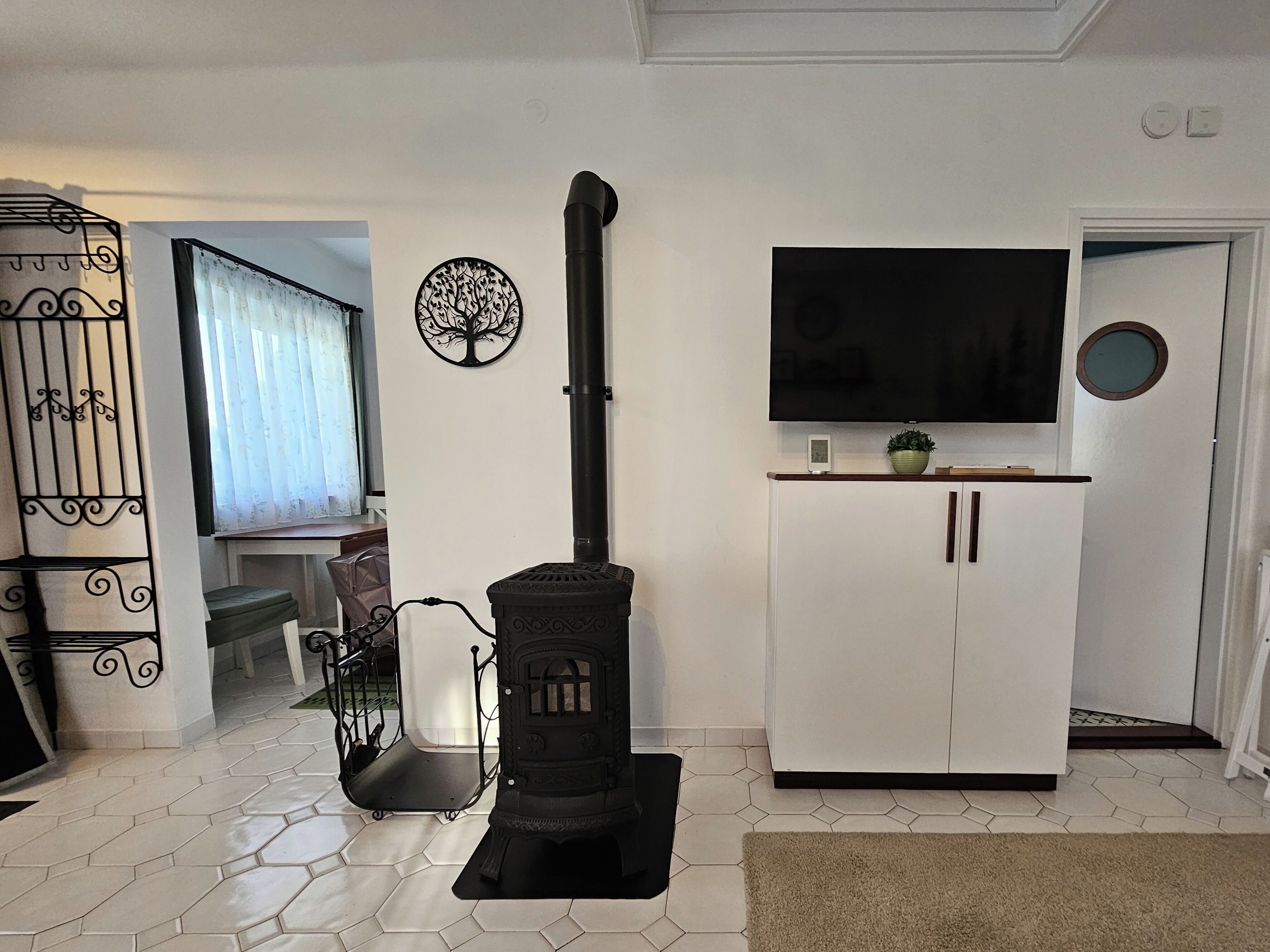 A living room with a black wood-burning stove, a white cabinet, a TV, and a decorative tree wall piece.