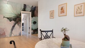 Uma área de refeições com uma mesa redonda, cadeiras, um vaso de planta e quadros nas paredes.