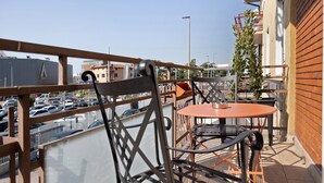 Varanda com cadeiras e mesa de metal, com vista para um estacionamento e edifícios.