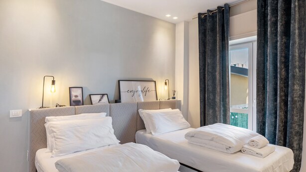 A hotel room with two beds, a headboard with a light fixture, a framed picture, and a window with curtains. - Suite Arena with Spacious Private Terrace (Verona)