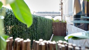 A garden area with a hedge, bamboo fence, and a building with a solar panel roof in the background. - Giulietta Suite with Private Bathroom, Balcony, Wi-Fi, and Air Conditioning (Verona)